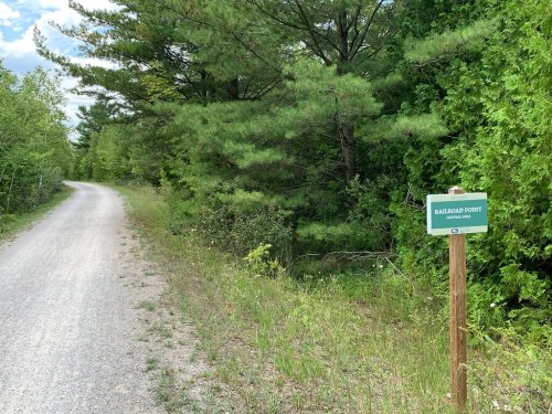 A gravel path lined with greenery, featuring a sign that reads "Railroad Point" on a wooden post.
