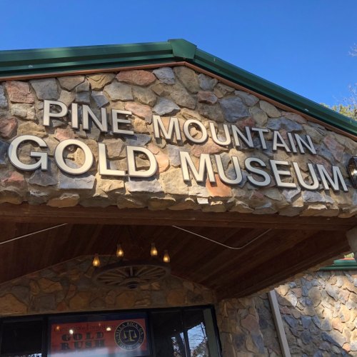 Sign for Pine Mountain Gold Museum, featuring stone architecture and clear blue sky above.