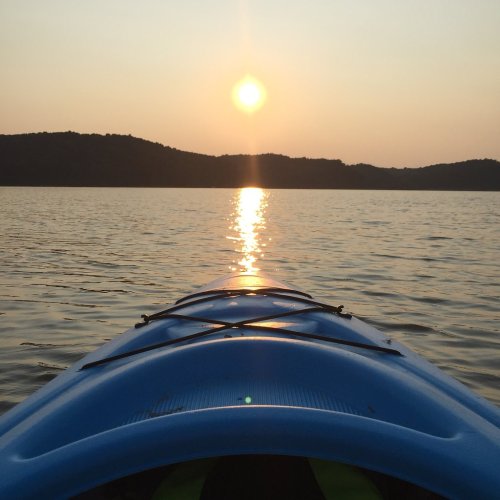 A blue kayak on calm water, with a sunset reflecting on the surface and hills in the background.