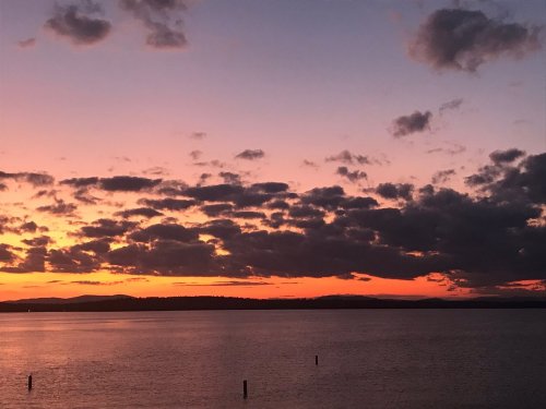 A vibrant sunset over a calm body of water, with colorful clouds reflecting orange and purple hues in the sky.