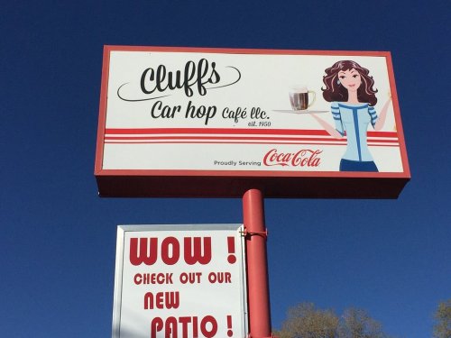 Sign for Cluffs Car Hop Café featuring a woman holding a drink, with a "Wow! Check out our new patio!" message below.