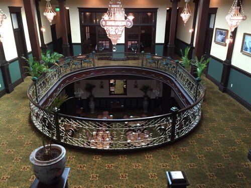 A grand interior view of a two-level space with ornate chandeliers, lush plants, and elegant railings.