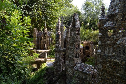 A whimsical garden scene featuring intricate stone and shell structures resembling castles, surrounded by lush greenery.