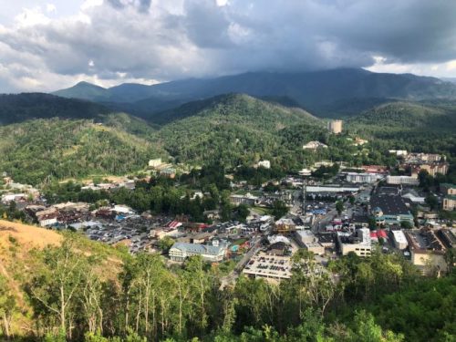 Aerial view of a mountainous town surrounded by lush greenery and buildings, under a cloudy sky.