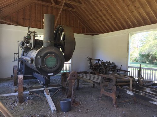 An old steam engine and machinery displayed in a wooden structure, showcasing vintage industrial equipment.