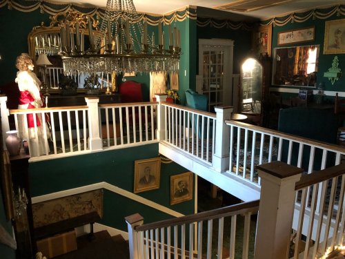 A vintage interior with a chandelier, green walls, and ornate decor, featuring a staircase and framed portraits.