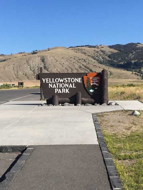 Sign for Yellowstone National Park with mountains in the background and clear blue sky.