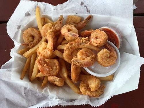 A basket of golden fried shrimp and French fries, served with a small cup of dipping sauce.