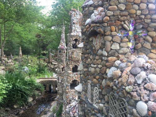 A whimsical garden featuring intricately designed stone towers adorned with shells and surrounded by lush greenery.