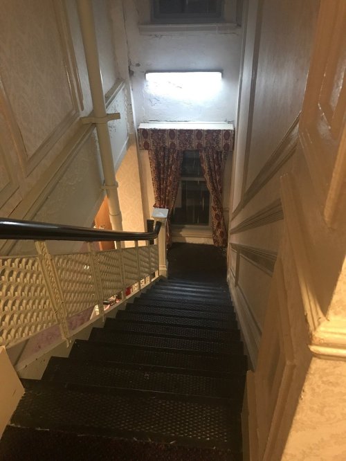 A dimly lit staircase with patterned wallpaper and a window at the bottom, leading down to a lower level.