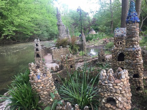 A whimsical stone castle landscape by a creek, surrounded by lush greenery and colorful decorations.
