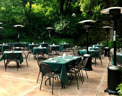 Outdoor dining area with green tables and chairs, surrounded by lush greenery and patio heaters.