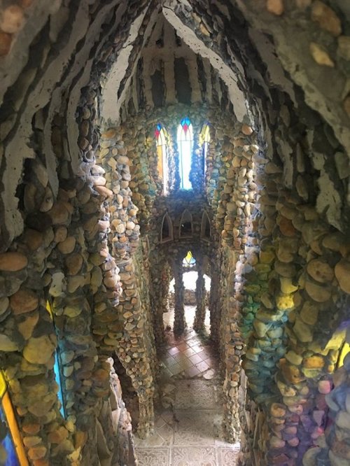 A stone interior with colorful stained glass windows, featuring a tall, narrow passageway and intricate rock walls.