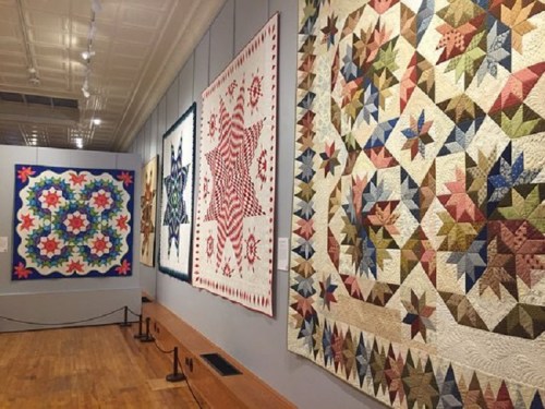 A gallery displaying colorful quilts with intricate patterns on the walls, showcasing textile art.