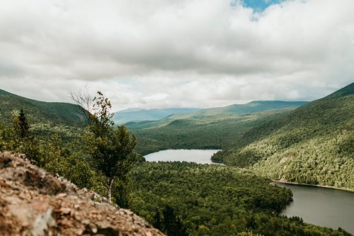 A scenic view of lush green mountains and a tranquil lake under a cloudy sky.