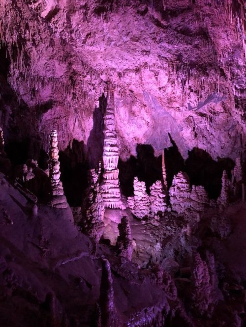 A colorful cave interior featuring tall, illuminated rock formations and stalagmites in shades of purple and pink.