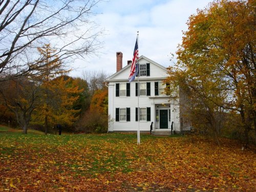 A white house with an American flag surrounded by colorful autumn foliage and fallen leaves.