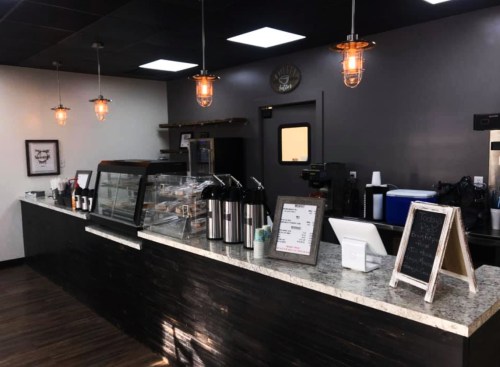 A modern coffee shop counter with a display case, menu board, and pendant lights, featuring a cozy atmosphere.