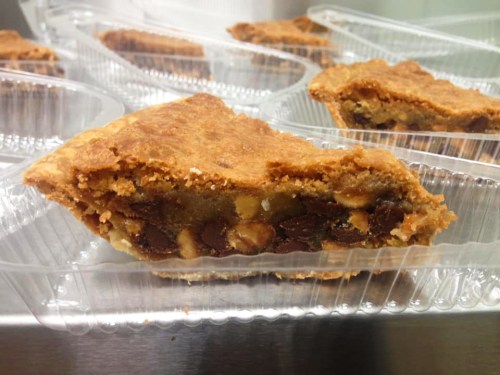 A slice of chocolate chip cookie pie in a clear plastic container, showcasing a golden-brown crust and chocolate chunks.