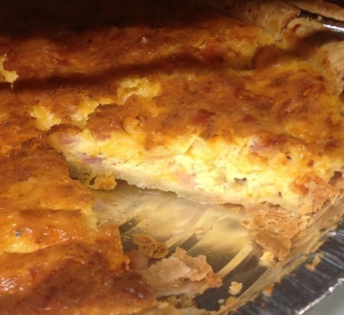 A close-up of a golden-brown quiche with a flaky crust, showing a slice removed to reveal the filling.