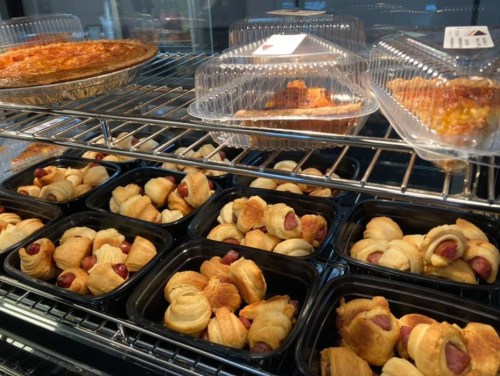 A display case filled with baked goods, including pastries and hot dog rolls in black containers.