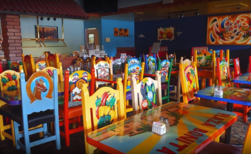 Colorful, hand-painted chairs and tables in a vibrant restaurant interior, featuring a lively Mexican theme.