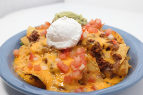 A plate of nachos topped with melted cheese, ground meat, diced tomatoes, guacamole, and a dollop of sour cream.