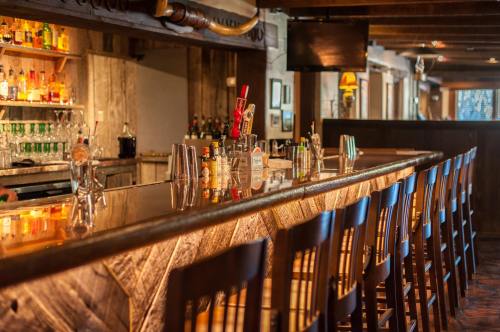A rustic bar with wooden stools, a polished countertop, and shelves stocked with various bottles of liquor.