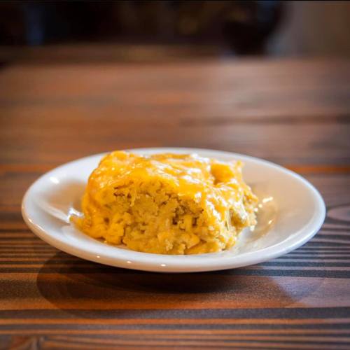A serving of cheesy cornbread on a white plate, resting on a wooden table.