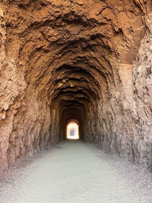 A rocky tunnel with textured walls, leading to a bright opening at the far end.