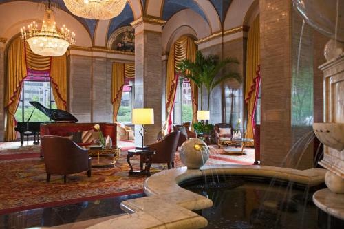 Luxurious hotel lobby with elegant seating, a grand piano, chandeliers, and a decorative fountain.
