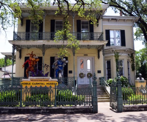 Historic yellow building with green shutters, featuring carnival figures and a sign for the Mobile Carnival Museum.