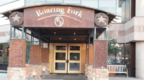 Entrance of Roaring Fork restaurant featuring wooden doors and rustic decor with star motifs.