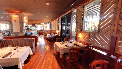 Interior of a cozy restaurant featuring wooden decor, tables set for dining, and large windows for natural light.