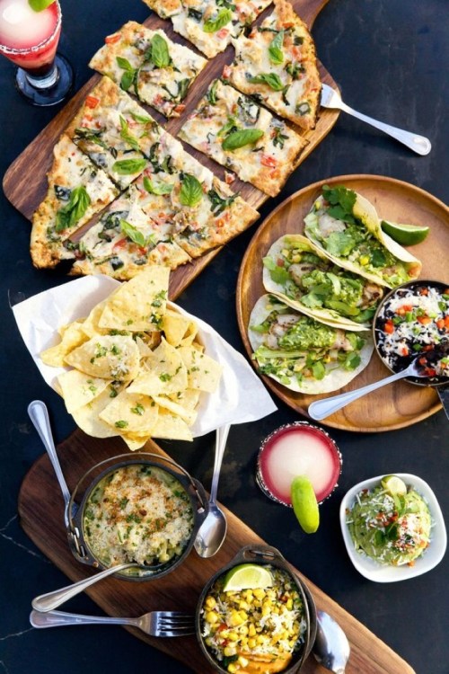 A spread of delicious dishes including pizza, tacos, nachos, and salads, with drinks in the background.