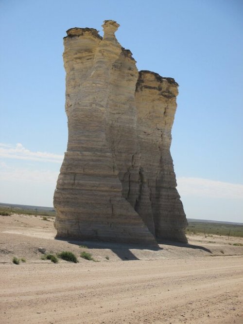 Two tall, eroded rock formations rise against a clear blue sky in a desert landscape.