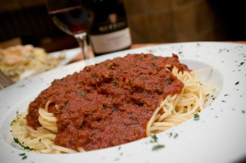 A plate of spaghetti topped with rich marinara sauce, garnished with herbs, alongside a glass of red wine.