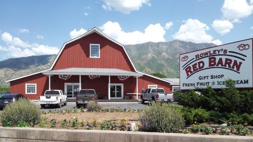 A red barn-style building with a sign for Rowley's Red Barn, featuring a gift shop and ice cream, surrounded by mountains.
