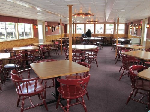 Interior of a dining area with wooden tables and red chairs, featuring large windows and a cozy atmosphere.