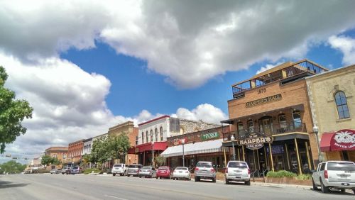 A charming street lined with historic buildings, shops, and restaurants under a partly cloudy sky.