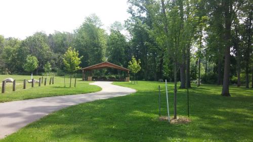 A winding path leads to a wooden pavilion surrounded by lush green trees and grass in a sunny park.