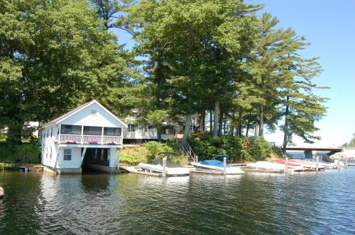 A serene lakeside scene featuring a white boathouse, colorful boats, and lush green trees under a clear blue sky.