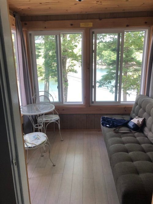 Cozy room with a gray sofa, small table, and large windows overlooking a lake and trees.