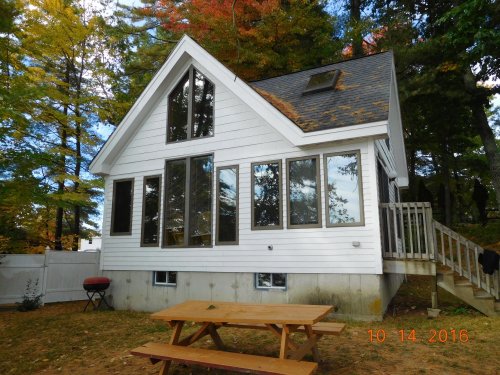A white house with large windows, surrounded by trees, and a picnic table in front on a sunny day.
