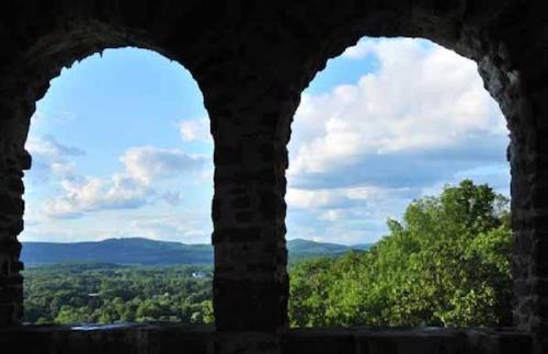 View through two stone arches overlooking a lush green landscape and blue sky with scattered clouds.