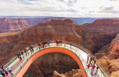 A glass bridge extends over the Grand Canyon, with visitors enjoying the stunning views of the rocky landscape below.