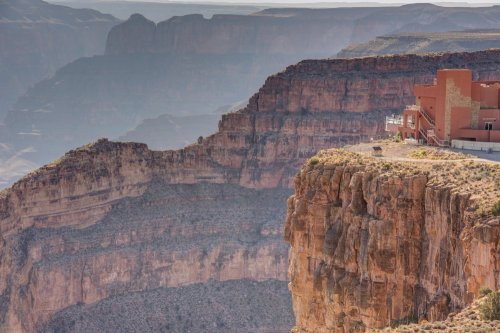A panoramic view of the Grand Canyon, showcasing layered rock formations and a distant building on the cliff edge.