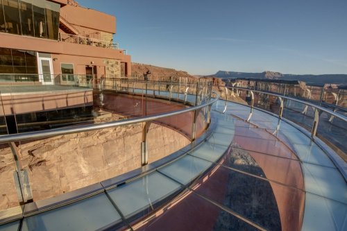 A glass walkway extends over a canyon, offering stunning views of the landscape and nearby cliffs.