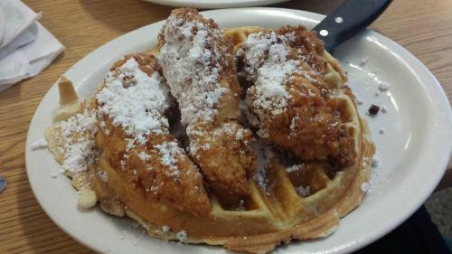 A plate of waffles topped with three pieces of fried chicken and dusted with powdered sugar.