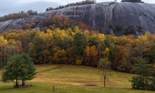 A large rock formation towers over a colorful autumn landscape with trees in shades of yellow, orange, and green.